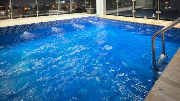 Ein Dachpool mit Glasgeländer, umgeben von einer weißen Struktur mit Glasscheiben und einem Blumentopf.
