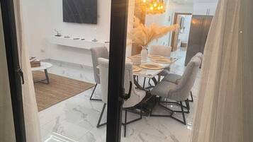 Una sala de estar moderna con una puerta corredera de vidrio, un comedor con mesa blanca y sillas grises, y una lámpara colgante original.