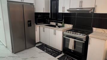 A modern kitchen with white cabinets, a stainless steel refrigerator, a black stove, and a black microwave.