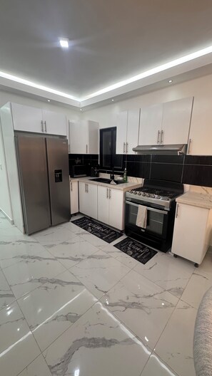 Een moderne keuken met witte kasten, een roestvrijstalen koelkast, een zwarte kookplaat en een zwarte magnetron.