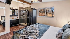 Quarto com cama, closet espaçoso, banheiro com chuveiro e janela com vista para árvores.