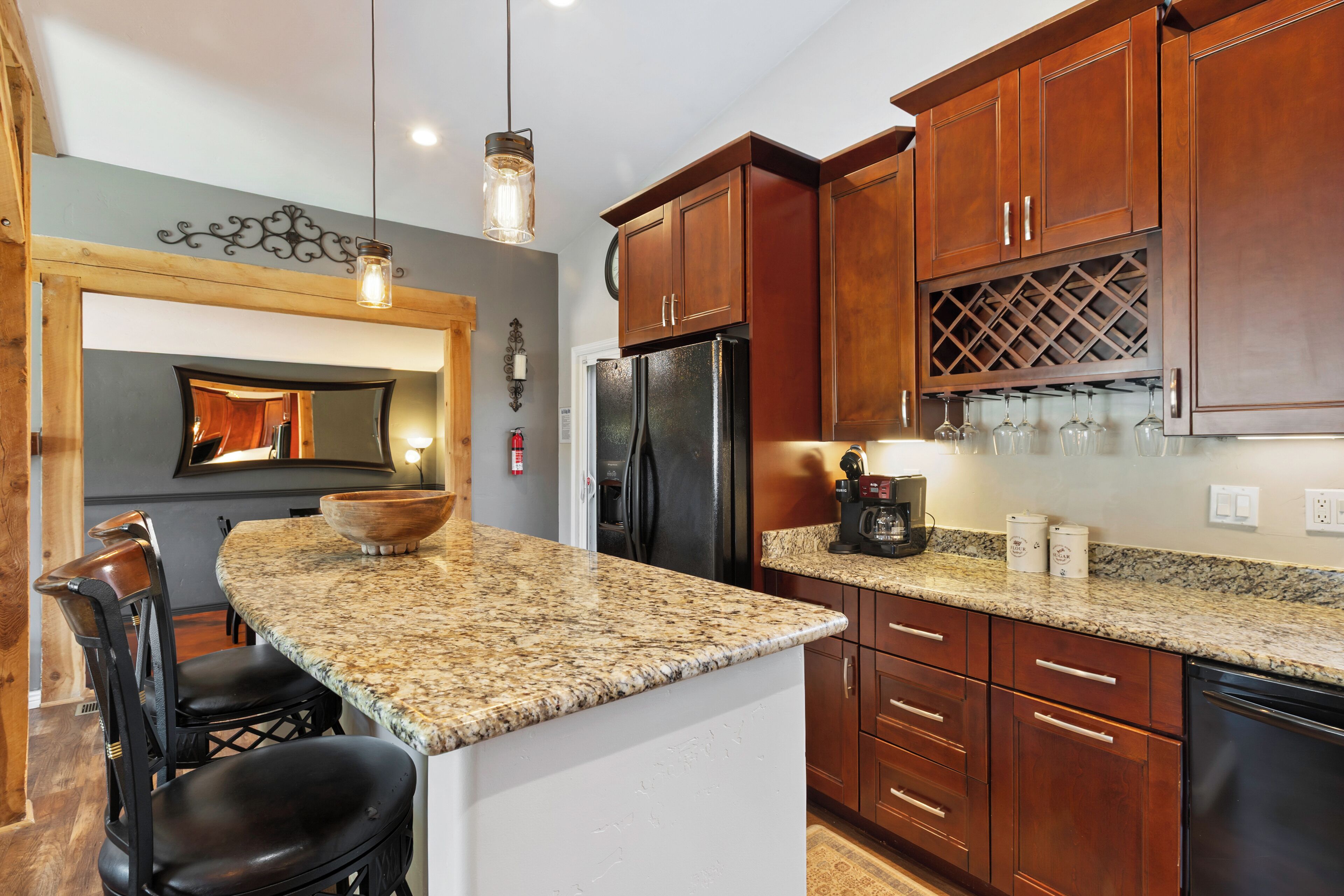 A kitchen with granite countertops, wooden cabinets, a refrigerator, and a wine rack.