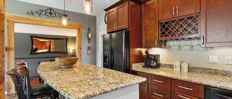 A kitchen with granite countertops, wooden cabinets, a refrigerator, and a wine rack.