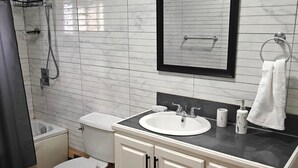 A bathroom with a toilet, sink, mirror, and shower.