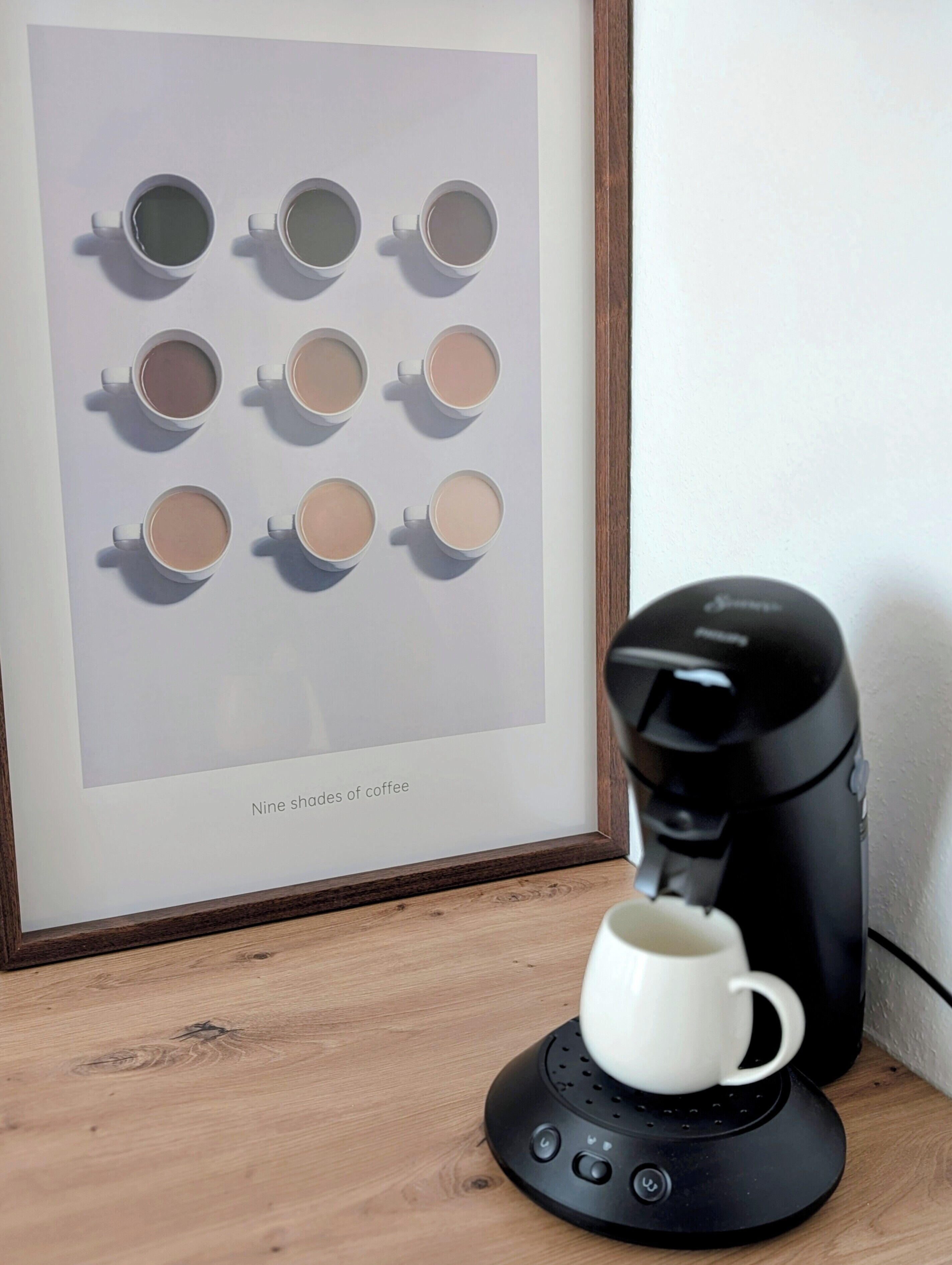 Un'opera d'arte incorniciata intitolata “Nine shades of coffee” su una superficie in legno, accanto a una macchina da caffè.