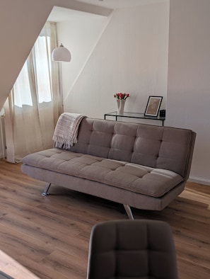 A modern living room with a sofa, a glass coffee table, and a small side table with a vase of flowers.