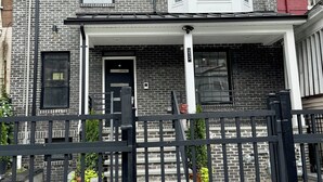 A two-story brick house with a front porch, a bay window, and a black metal gate. - Marvelous 3-bedroom/2 bath  apartment with AC in vibrant Newark (Newark)