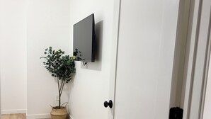 A hallway with a wooden floor, a white door, a mounted television, and a potted plant. - Marvelous 3-bedroom/2 bath  apartment with AC in vibrant Newark (Newark)
