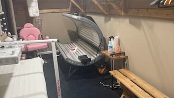 A room with a massage chair, a massage table, a wooden bench, and a shelf with a box labeled 'PLATINUM LIGHTS'.