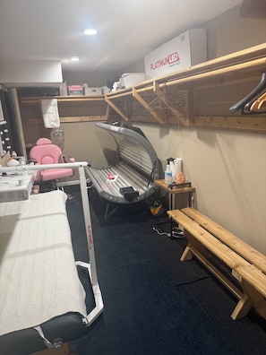 Ein Zimmer mit Massagesessel, Massageliege, einer Holzbank und einem Regal mit einer Kiste mit der Aufschrift 'PLATINUM LIGHTS'.