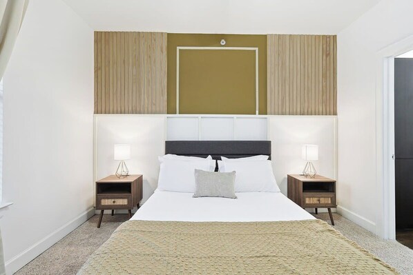 Une chambre à coucher avec un grand lit, deux tables de chevet et une tête de lit dotée d’un luminaire.