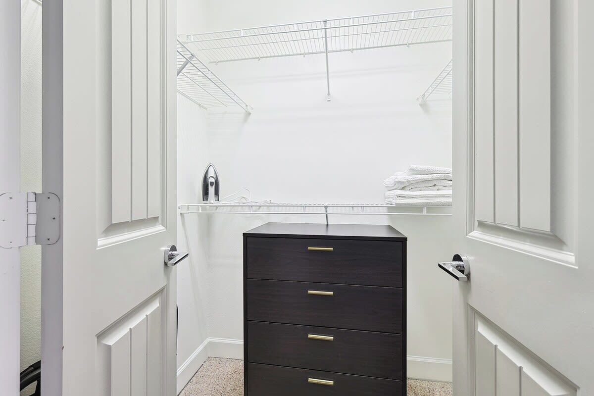 A white closet with a dark dresser and a metal shelf.
