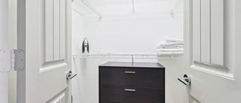 A white closet with a dark dresser and a metal shelf.