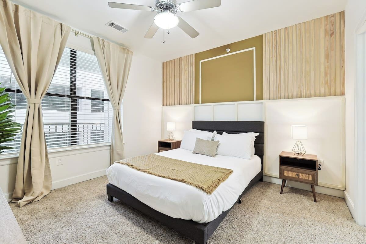 A bedroom with a bed, two bedside tables, a ceiling fan, and a window with curtains.