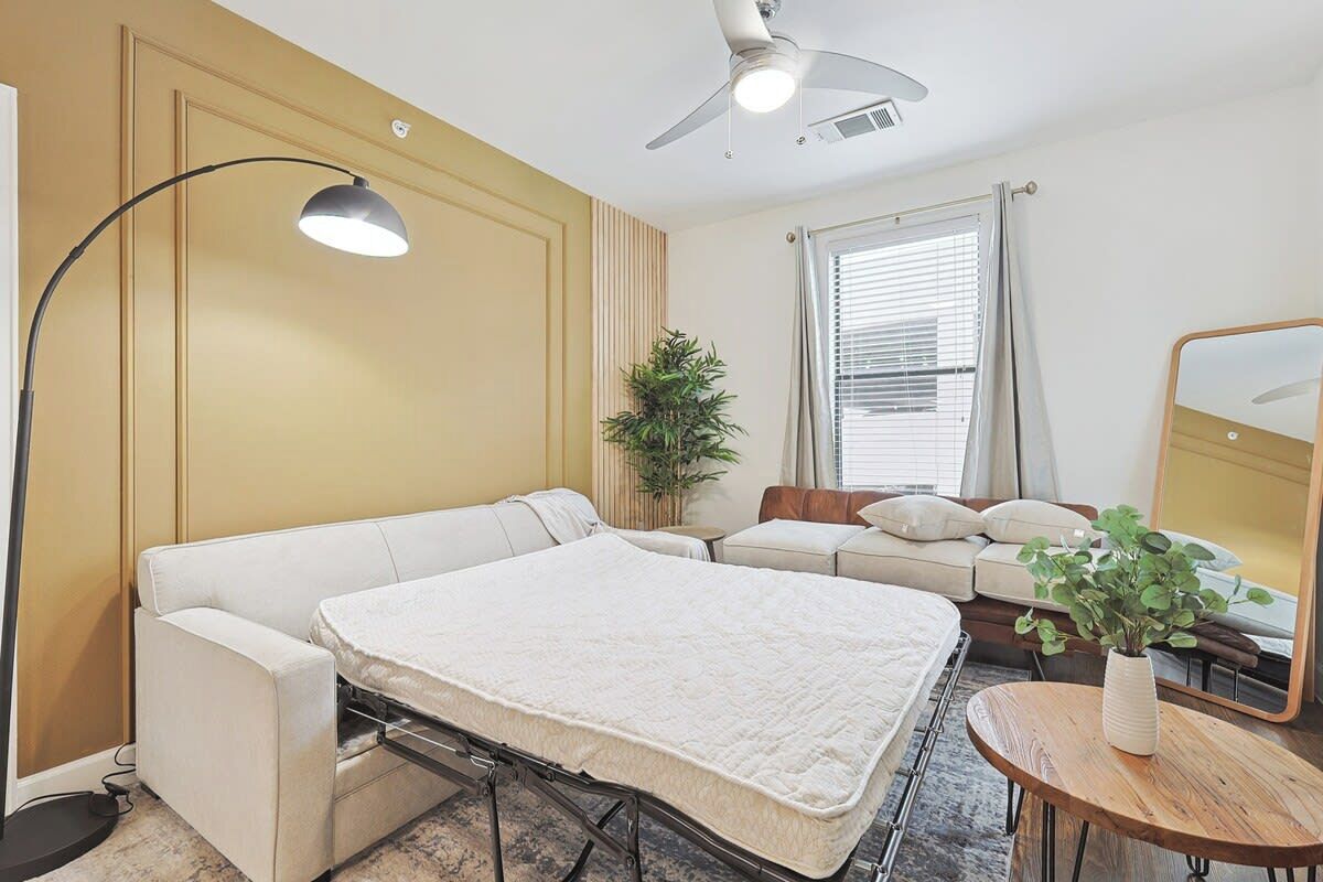 Una habitación con cama, escritorio, silla, planta y ventilador de techo.