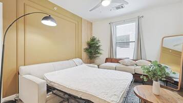 Una habitación con cama, escritorio, silla, planta y ventilador de techo.