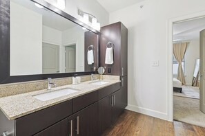 A modern bathroom with a large mirror, dark cabinetry, and a granite countertop. - Luxurious 2B2B Near Toyota HQ (Frisco)