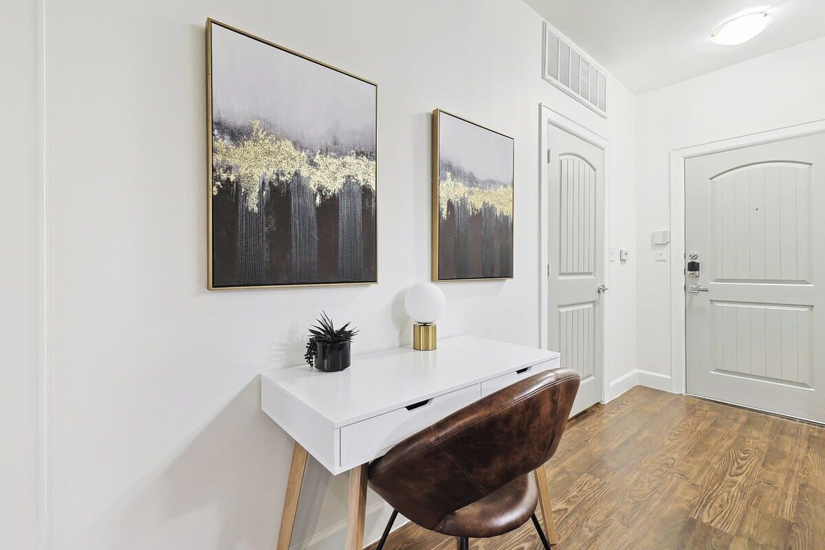 Een moderne kantoorruimte met een wit bureau, een bruine leren stoel en twee abstracte schilderijen aan de muur.