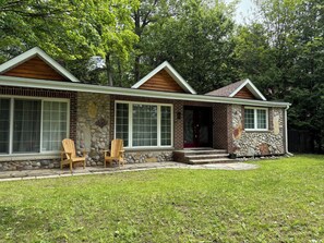 Une maison à deux étages avec une façade en pierre, de grandes fenêtres et un porche à l’avant, agrémenté de deux chaises en bois.