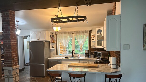 A kitchen with a marble countertop, a built-in island with stools, a refrigerator, a stove, and a hanging light fixture. - The Quinta at Balm Beach (Perkinsfield)