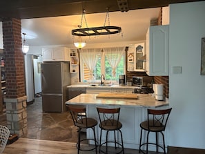 A kitchen with a marble countertop, a built-in island with stools, a refrigerator, a stove, and a hanging light fixture. - The Quinta at Balm Beach (Perkinsfield)