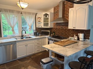 Una cocina moderna con armarios blancos, estufa integrada, microondas y un ventanal con cortinas ligeras.