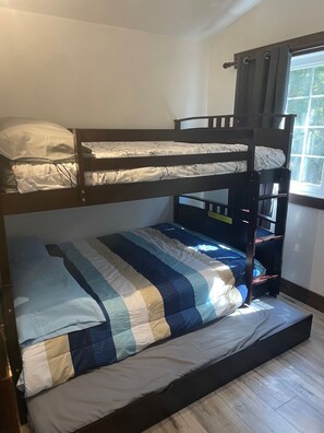 Une chambre avec un lit superposé, une fenêtre, un plancher en bois et une couvre-lit à rayures.