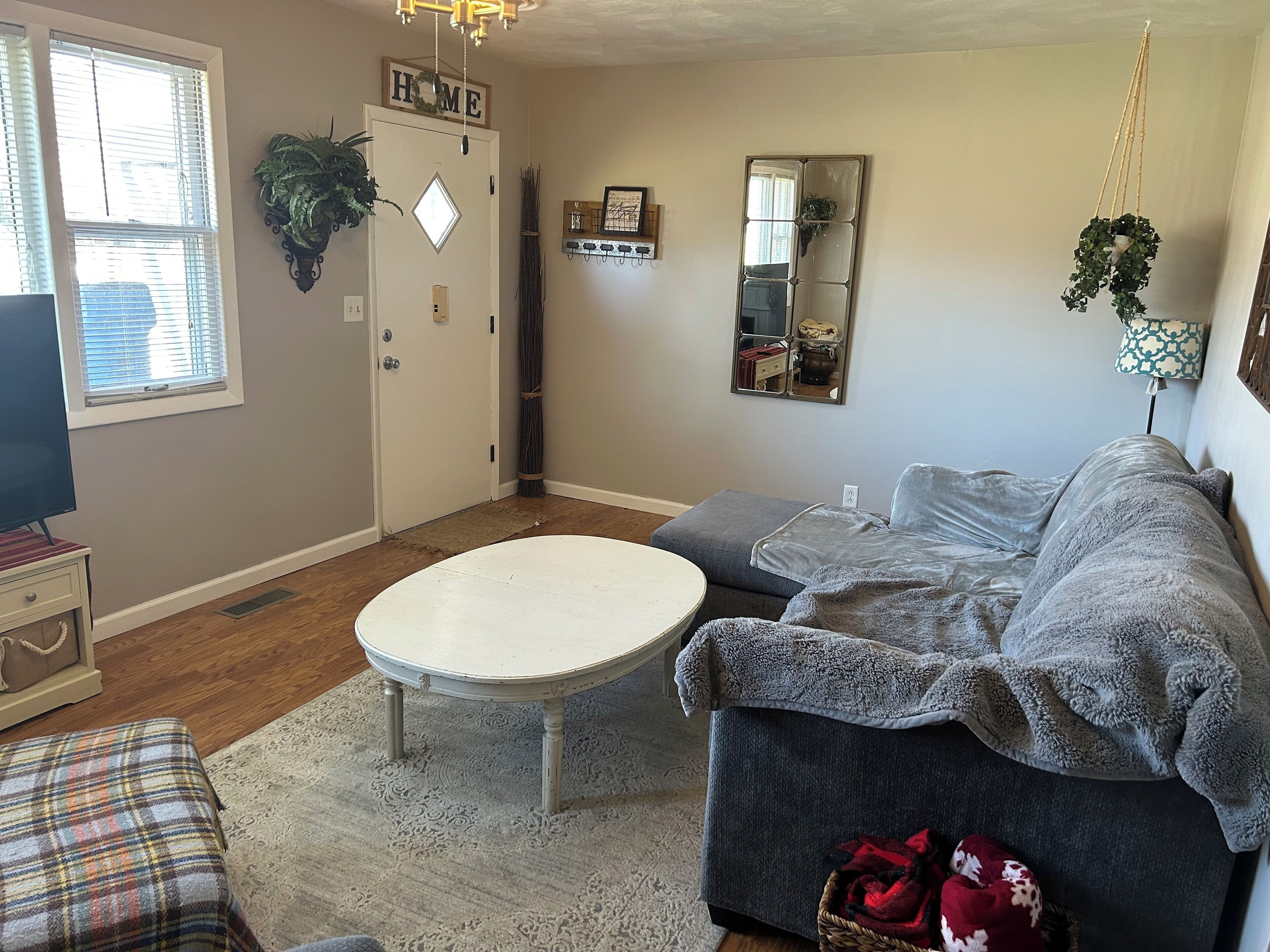 A living room with a gray sofa, a white coffee table, and a plaid ottoman.