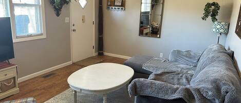 A living room with a gray sofa, a white coffee table, and a plaid ottoman.