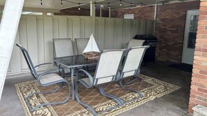 Um pátio externo com mesa, cadeiras, churrasqueira e uma vela decorativa.