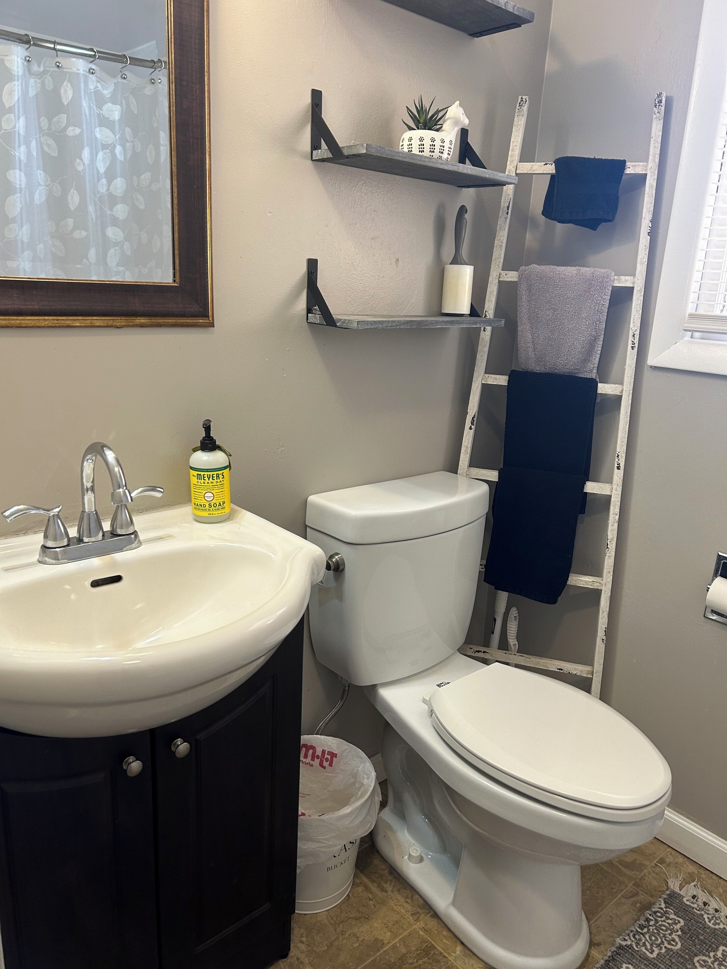 A bathroom with a white sink, toilet, and a shelf with a plant and a towel.
