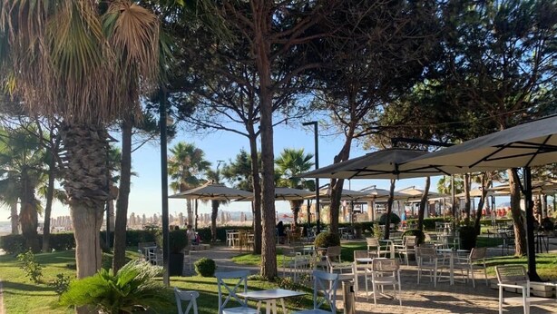 Un espace extérieur aménagé en terrasse, avec des tables et des chaises, entouré d’arbres et offrant une vue sur les bâtiments de la ville.