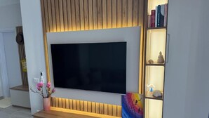 Un meuble de divertissement moderne, doté d’un téléviseur à écran plat, de panneaux en bois et d’une étagère où sont disposés des objets décoratifs.