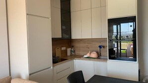 Une cuisine de taille réduite, avec des meubles blancs, un plan de travail en bois et une fenêtre donnant sur l’extérieur.