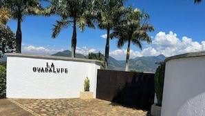 A gated entrance with a sign reading "LA GUADALUPE" and a stone-paved area with palm trees and mountains in the background. - Finca La Guadalupe - The Pearl of the Southwest (Tarso)
