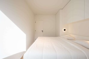 Ein schlicht eingerichtetes Schlafzimmer mit einem großen Bett, einer Tür und einer Wandleuchte.