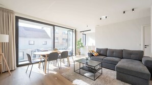 Ein modernes Wohnzimmer mit grauem Sofa, Couchtisch und Essbereich mit Stühlen und Tisch.