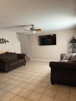 A living room with a ceiling fan, two sofas, a TV mounted on the wall, and a staircase leading upstairs. - 2-bedroom townhome in pleasant Harlingen. Sleeps 6  (Harlingen)
