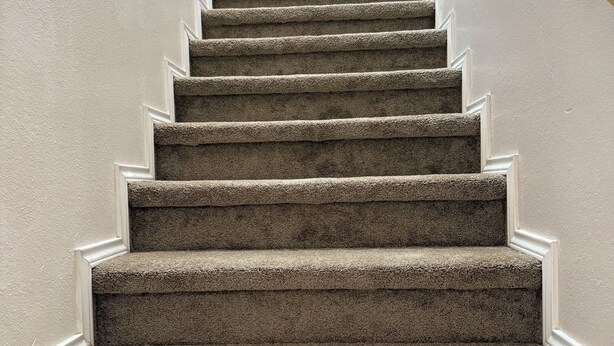 Eine Teppichstufen-Treppe mit weißer Umrandung und einem Geländer auf der rechten Seite.