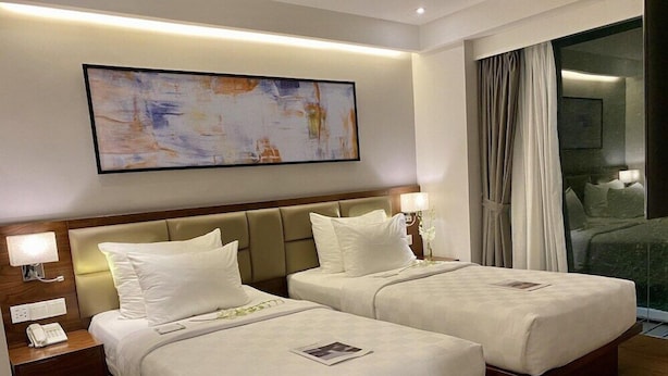 Habitación de hotel con dos camas, una mesita de noche con teléfono, un cuadro en la pared y vista a un balcón.