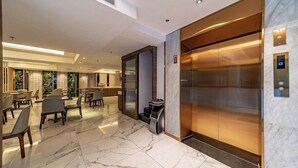 Un moderno hall de hotel con suelo de mármol, mostrador de recepción, zona de estar y ascensor.