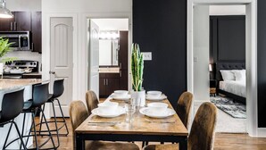 Une cuisine moderne avec des meubles de couleur sombre, un four à micro-ondes et une cuisinière. On y trouve également un coin repas avec une table en bois, des chaises et une plante en pot.