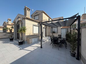 Eine Dachterrasse mit Tisch und Stühlen, Kübelpflanzen und einer Pergola.
