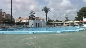 En swimmingpool med en livräddarstation, omgiven av palmer och byggnader.