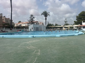 A swimming pool with a lifeguard station, surrounded by palm trees and buildings. - 70-square-meter house / sleeps 6 / 50-meter community pool (Torrevieja)