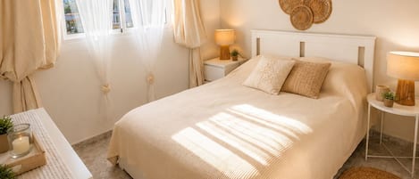 A bedroom with a large bed, bedside tables, a bedside lamp, a small plant, and a window with curtains.