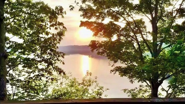 Vista desde una terraza de madera con vistas a un lago, con árboles enmarcando el paisaje.