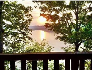 Une vue depuis une terrasse en bois donnant sur un lac, avec des arbres qui encadrent le paysage.