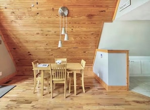 Une pièce avec un plafond en bois, une table à manger avec des chaises et un petit meuble.