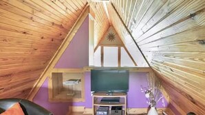 Un acogedor dormitorio en ático con vigas de madera, pared morada, un televisor sobre un mueble de madera y una mesita pequeña.
